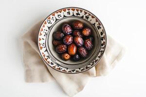 A decorative bowl filled with dates rests on a beige napkin photo