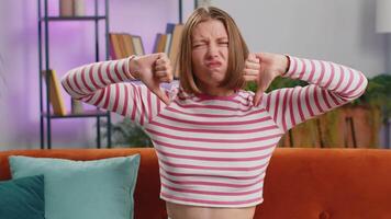 Dislike. Portrait of upset brunette woman showing thumbs down sign gesture, expressing discontent, disapproval dissatisfied bad work at modern home apartment indoors. Displeased girl in room on sofa video