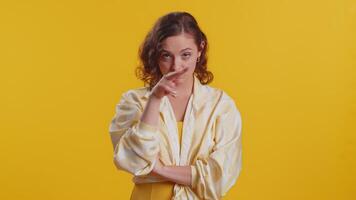 I am watching you. Young confident woman pointing at her eyes and camera, show I am watching you gesture, spying on someone. Pretty attractive brunette girl isolated alone on yellow studio background video