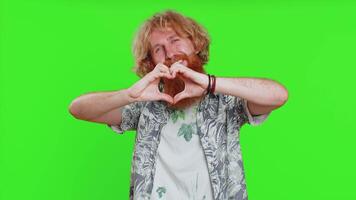 Man in love. Smiling attractive bearded man makes heart gesture demonstrates love sign expresses good positive feelings and sympathy. Handsome redhead young guy isolated on chroma key wall background video