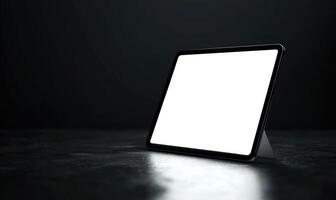 A tablet is sitting on a dark surface with a white screen photo