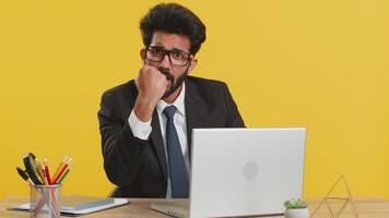 Aggressive angry indian businessman trying to fight at camera, shaking fist, boxing with expression, punishment, quarrel at office workplace. Hindu man working on laptop isolated on yellow background video