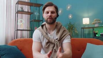 POV of Caucasian man wearing headset, freelance worker, call center or support service operator helpline, having talk with client or colleague communication support waving hello. Guy at home room video
