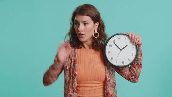Woman with anxiety checking time on clock, running late to work, being in delay, deadline. Brunette busy girl looking at hour, minutes, worrying to be punctual isolated on blue studio background video