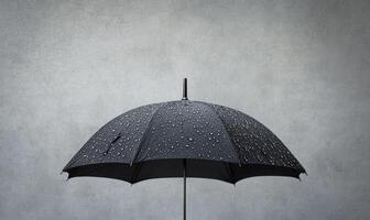 A black umbrella is open and has raindrops on it, gray wall background photo