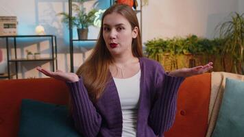 I dont know what to say. Confused pretty woman feeling embarrassed about ambiguous question, having doubts, no idea, being clueless and uncertain at home. Portrait of girl sits on sofa in living room video