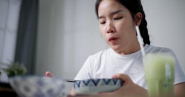 Handheld low angle view shot, Young Asian woman is sitting at a dining table, enjoying a bowl of noodles with chopsticks video
