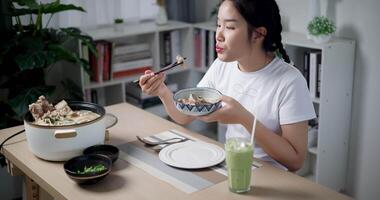 Handheld high angle view shot, Asian woman is happily eating noodles at the dining table at home. Enjoy a meal at home video