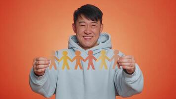 Man showing multiracial different skin color human shape cut out of paper, concept of teamwork, partnership, community, unity, people support love against racism. Asian guy on orange studio background video