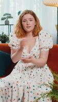 What. Why. Woman raising hands in indignant expression asking reason of failure demonstrating disbelief irritation by troubles at modern home apartment. Redhead girl in room sitting on sofa. Vertical video