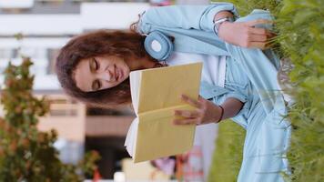 Preteen child kid relaxing interesting education story book turning pages smiling enjoying literature taking a rest. Portrait of peaceful cheerful girl sitting on grass in city park outdoors. Vertical video