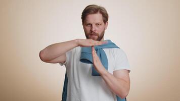 Tired serious upset young caucasian man showing time out gesture, limit or stop sign, no pressure, I need more time, relax, break, deadline. Handsome guy isolated on studio beige background indoor video