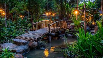 Serene Bamboo Bridge at Dusk in a Tropical Garden. A tranquil scene of a wooden bridge over a pond, illuminated by warm lamplight. photo