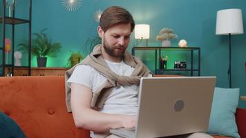 Caucasian man sitting on couch closing laptop after finishing work in living room. Young guy freelancer working online, remote job at home sofa. E-learning, browsing internet on notebook computer video