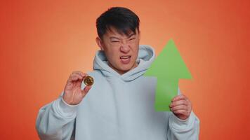 Asian man show golden bitcoins indicating up arrow sign successful exchange rate increase. Achievement career wealth, cryptocurrency investment mining BTC future technology. Guy on orange background video