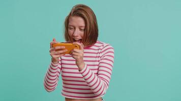 Worried funny addicted woman enthusiastically playing racing games on mobile phone. Happy girl in crop top using smartphone gadget app with drive simulator isolated on blue studio background video