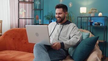Caucasian man sitting on couch looking at camera, making webcam conference call with friends or family, enjoying pleasant conversation. Young guy laughing waving hello at home room apartment video