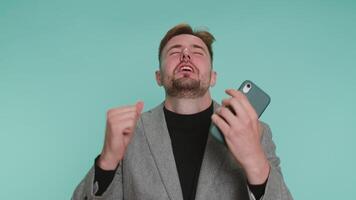 Bearded business man use mobile cell phone typing browsing, loses becoming surprised sudden lottery results, bad fortune, loss, fail. Young adult guy boy isolated alone on blue studio wall background video