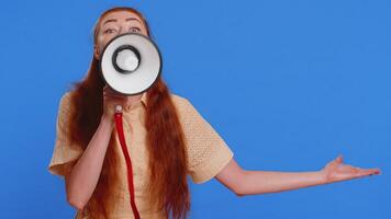 Woman talking with megaphone, proclaiming news, loudly announcing advertisement, warning using loudspeaker to shout speech, pointing empty place. Copy-space. Pretty redhead girl on blue background video