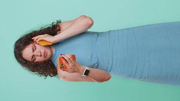 Irritated nervous stressed young woman talking screaming on two mobile phones having conversation conflict quarrel complaint dispute discuss solve problem. Girl on blue studio background. Vertical video