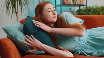 Tired young redhead woman lying down in bed taking a rest at home. Portrait of carefree girl napping, falling asleep on comfortable orange sofa with pillows. Closed her eyes enjoy daytime nap alone video