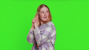 Young woman pointing around with finger gun gesture, looking confident, making choice, shooting killing with hand pistol right on target. Girl isolated on green chroma key background. Advertisement video