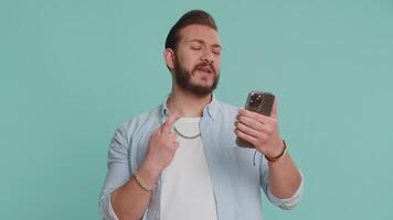 Lebanese man use mobile cell phone typing browsing, loses becoming surprised sudden lottery results, bad fortune, loss, fail. Handsome arabian guy isolated alone on blue studio wall background indoors video
