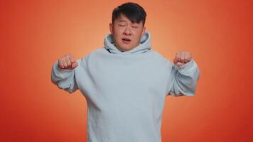 Tired asian handsome man yawning, sleepy inattentive feeling somnolent lazy bored gaping suffering from lack of sleep. Adult guy isolated alone on orange studio background. People lifestyle concept video