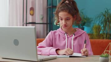 Tired Caucasian preteen school girl sleeping on laptop computer with eyes stickers on face. Young lazy child, kid cheating to sleep at home workplace sitting at the table. Distance learning education video