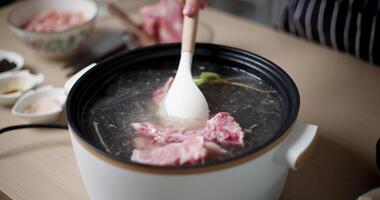 Handheld selective focus shot, A young woman is using a spatula to stir soup in an electric pot. video