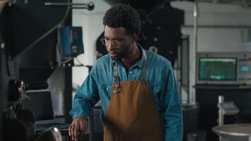 African American man working roasted coffee beans using industrial roasting machine checking confused male roaster in apron guy hands crossed arms posing smiling at modern factory professional barista video