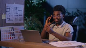 African American business man designer architect businessman talk mobile phone in night office busy guy manager engineer online laptop work overtime evening call consulting discuss architecture plan video