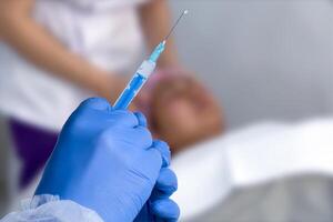 Cosmetologist in sterile gloves holds syringe for injection with collagen hyaluronic filler for face or lips rejuvenation, close up. photo