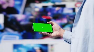 Young adult checks green screen on phone as a user interface, checking online presence on social platforms. Male Influencer working on creativity and online engagement in a digital world. Camera A. video