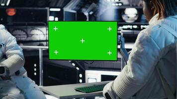 Astronaut reviewing onboard analytics on green screen monitor before stepping outside space station. Cosmonaut verifying parameters on mockup display after landing on planet, camera B video