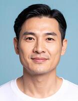 Portrait of a smiling Asian man against a serene blue backdrop, showcasing his calm and friendly expression. photo