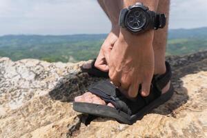 A person is adjusting their sandals outdoors on a rocky surface, with a watch visible on their wrist. photo