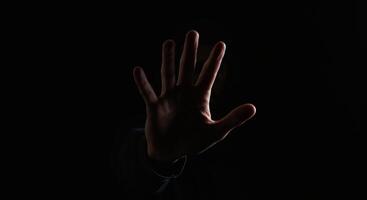 hand emerging from darkness, palm outstretched in a stop gesture, dramatically lit, conveying refusal or warning. photo