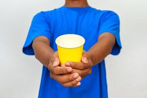 Close-up of a person offering a yellow paper cup with both hands, inviting you to drink photo