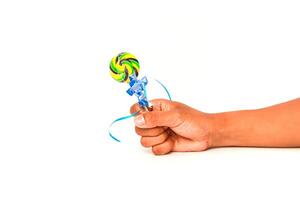 A child's hand holds a vibrant lollipop with a blue ribbon against white photo