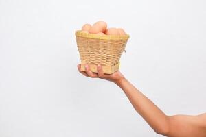 Hand Holding a Woven Basket of Brown Eggs Against a White Background photo