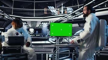 Astronauts in advanced technology spacecraft using green screen monitor updating flight log during routine mission check. Orbit station crew colleagues looking at system diagnostics on mockup display video