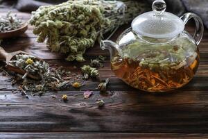 Tea is steeping in glass teapot, surrounded by fresh herbs and dried flowers on weathered wooden table, creating warm and inviting atmosphere for relaxation and enjoyment photo