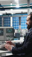 Vertical Male industry expert examining production data in a solar tech plant, ensuring innovation and efficiency to drive alternative energy success. Sustainable solutions for development. Camera A. video