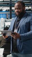 Vertical African american technician analyst in a solar manufacturing plant evaluates operations, dressed in suit to reflect corporate oversight and equipment manufacturing. Clean energy. Camera A. video