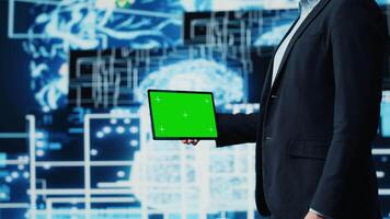 Business AI expert holding green screen on device next to brain animation, ensures implementing neural networks system. Young specialist analyzing algorithms and coding tools. Camera A. video