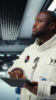 Vertical Astronaut analyzing planetary data in spacecraft powered by advanced engineering. African american starship crew member exploring deep space, doing surface research, camera A video