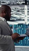 Vertical Server room infrastructure engineer scripting automated workflows using software on laptop. Data center programmer running predictive maintenance scans using notebook, camera A video