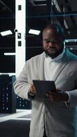 Vertical Admin in data center using tablet to develop disaster recovery plans. IT expert walking in server farm, testing failover scenarios, protecting data during disruptions, camera A video
