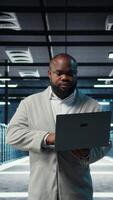 Vertical Data center computer scientist using laptop to manage system stability. Server room IT professional optimizing performance with device, configuring equipment rigs, camera A video